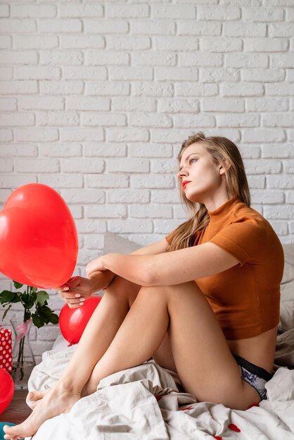 Celebrazione del matrimonio di San Valentino e del giorno dell'amore della donna. Bella donna che tiene un palloncino rosso a forma di cuore seduto a letto