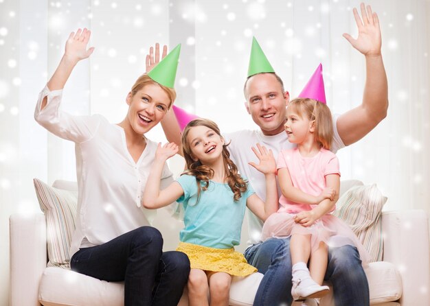 celebrazione, famiglia, vacanze, gesto e concetto di persone - famiglia felice con due bambini in cappelli da festa che agitano le mani a casa