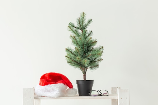 Celebrazione, vacanze invernali e concetto di pubblicità - piccolo albero di Natale e cappello della santa sul muro bianco.