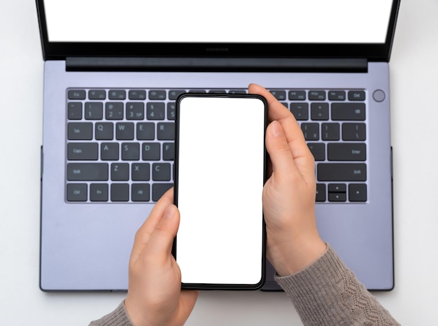 Cellulare mockup Immagine mockup vista dall'alto di mani che tengono un telefono cellulare con schermo bianco vuoto con computer portatile