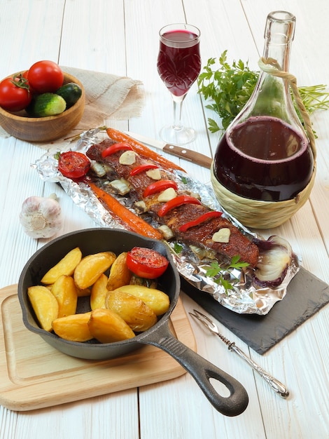 Cena di campagna - costolette di vitello arrosto con verdure, patate e vino rosso su un tavolo di legno bianco