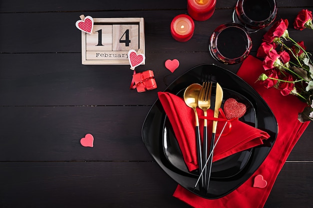 Cena di San Valentino con tavola con regalo, rose rosse, cuori con due bicchieri di vino sul buio
