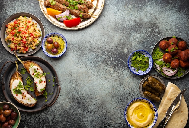 Cena mediorientale o mediterranea con kebab alla griglia, falafel, verdure arrosto e fresche, meze arabi assortiti e antipasti su tavola di fondo rustico. Tavolo da pranzo in alto, spazio per il testo