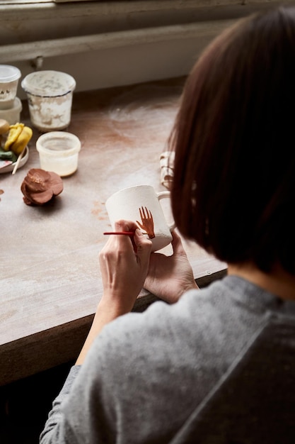 Ceramista femminile che lavora nello studio della ceramica. Le mani del ceramista sporche di argilla. Processo di creazione della ceramica. Il maestro ceramista lavora nel suo studio