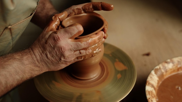 Ceramista non riconosciuto che produce prodotti in argilla in laboratorio Mani d'artista che lavorano con argilla bagnata sulla ruota del ceramista in studio Maestro sconosciuto che scolpisce prodotti in ceramica al rallentatore