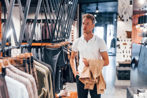 Cerca giacca Ragazzo giovane in un negozio moderno con vestiti nuovi Abbigliamento elegante e costoso per gli uomini