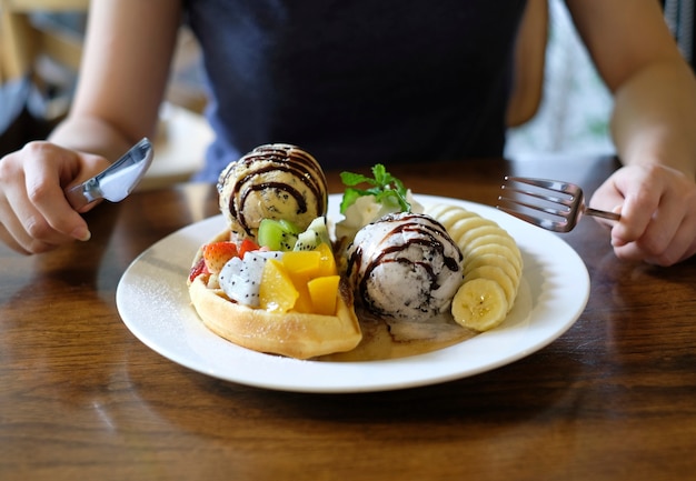 Cercando di usare forchetta e coltello per mangiare cialde servite con frutta mista, banana affettata