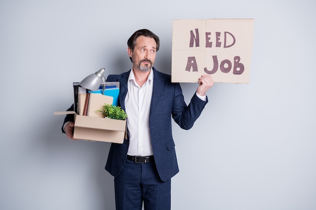 Cercare un lavoro. Foto di un lavoratore infelice ragazzo maturo crisi finanziaria lavoro perso tenere scatola di cartone oggetti personali smettere di tenere cartello banner ricerca posto di lavoro indossare tuta isolato sfondo grigio