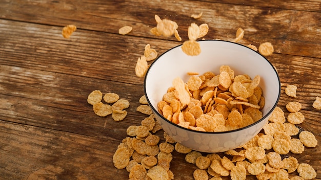 Cereali che cadono in una ciotola bianca su un tavolo di legno. Foto luminosa. Sana colazione veloce