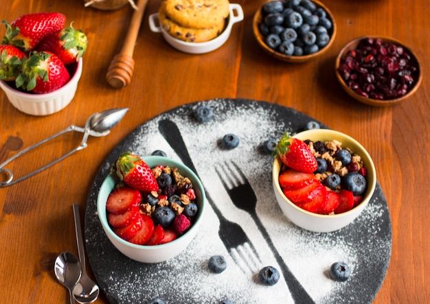 Cereali, colazione con muesli e frutta fresca in ciotole su un tavolo di legno rustico