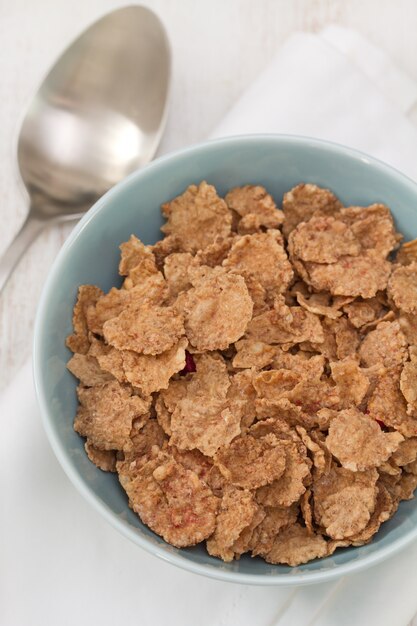 Cereali in ciotola blu sulla tavola e sul cucchiaio di legno bianchi