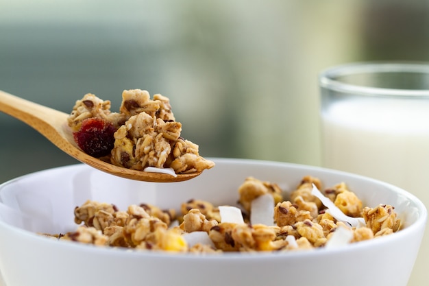 Cereali per la colazione a secco. Ciotola di muesli croccante al miele con semi di lino, mirtilli rossi, cocco e un bicchiere di latte da vicino. Alimenti sani, puliti e ricchi di fibre. Ora di colazione