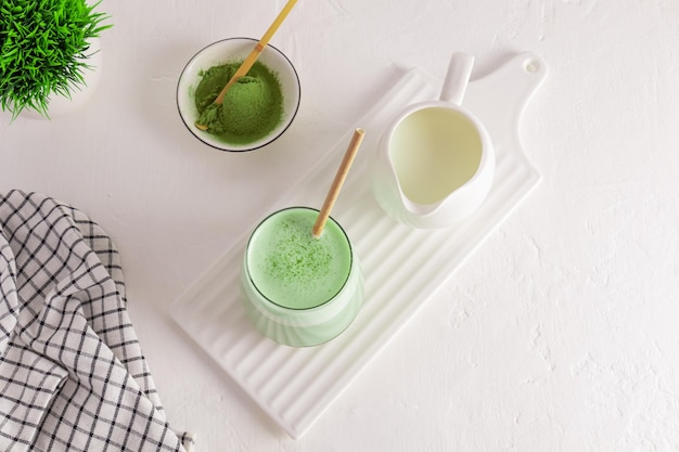 Cerimonia del tè matcha latte tè verde con latte in un bicchiere su una tavola di ceramica bianca una brocca di latte una ciotola di polvere verde un'alternativa al caffè