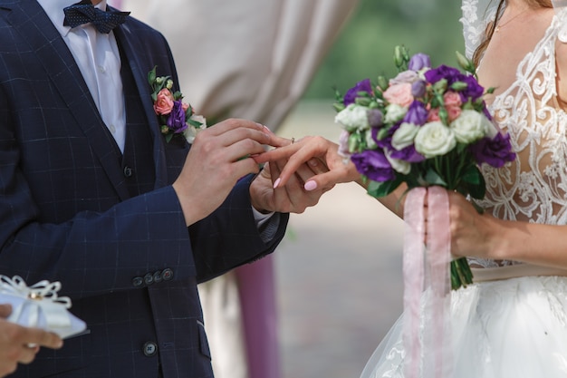 cerimonia di nozze all'aperto vicino. lo sposo indossa l'anello nuziale della sposa. giorno del matrimonio. sposi emotivi si stanno scambiando fedi nuziali. felice coppia appena sposata.