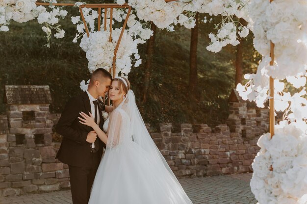 Cerimonia matrimoniale. Felice sposa, sposo e damigelle d'onore vicino al bellissimo arco di nozze