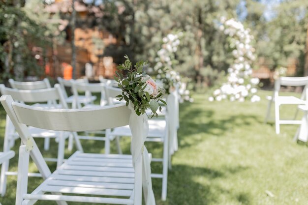 Cerimonia nuziale all'aperto con uno splendido arco floreale e sedie bianche disposte in un giardino sereno