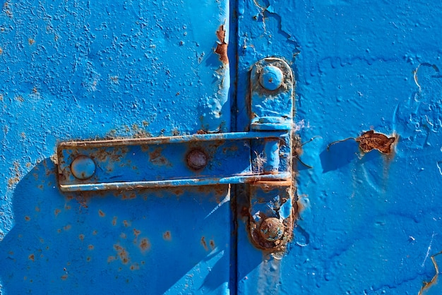 Cerniera arrugginita sulla vecchia porta arrugginita blu del metallo, primo piano