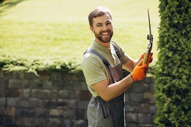 Cespugli di rifilatura del lavoratore del giardino con le forbici nel cortile