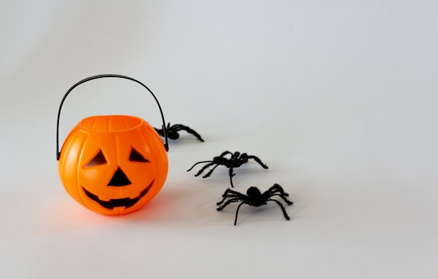 Cestino di caramelle a forma di lanterna di Halloween su sfondo bianco con ragni giocattolo Spazio di copia