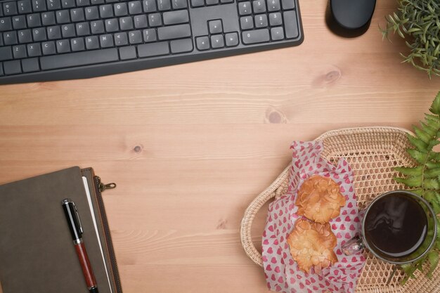 Cestino di vimini con biscotti e tazza di caffè sulla scrivania in legno.