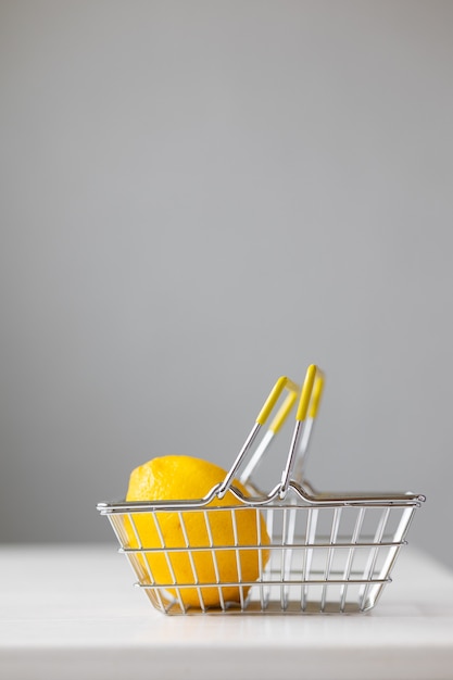 Cestino per alimenti in metallo per supermercati con banconote e monete al limone su un tavolo bianco