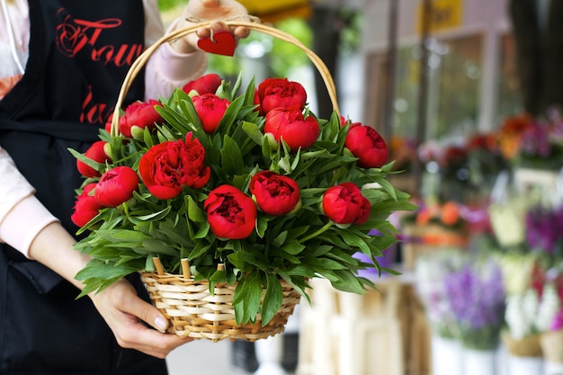 Cesto con peonie nelle mani del venditore di una boutique di fiori