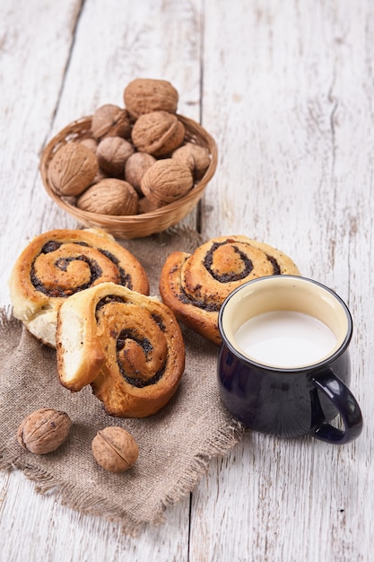 Cesto di focacce fatte in casa con marmellata, servito sul vecchio tavolo in legno con noci e tazza di latte