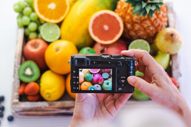 Cesto di legno sulla tovaglia bianca piena di frutta fresca cruda Donna caucasica matura che utilizza la macchina fotografica