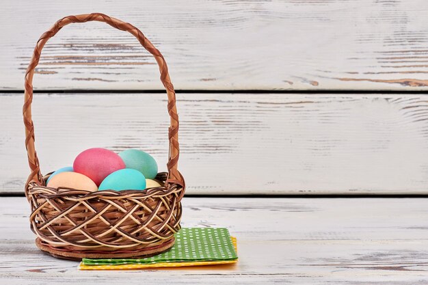 Cesto di uova di Pasqua e tovaglioli cesto di vimini bianco sullo sfondo di legno