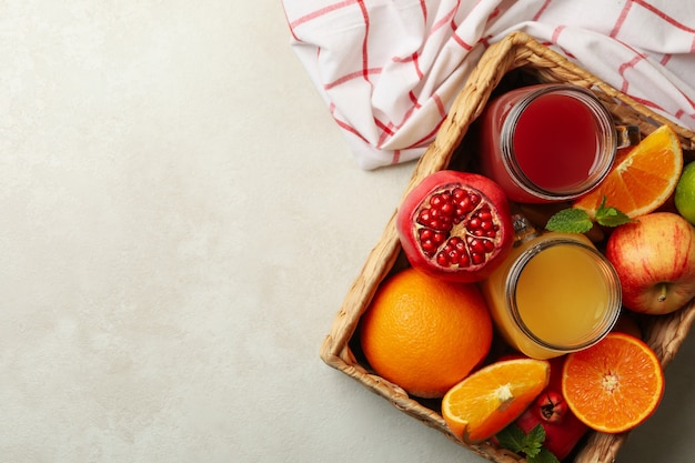 Cesto di vimini con diversi succhi di frutta sul tavolo bianco