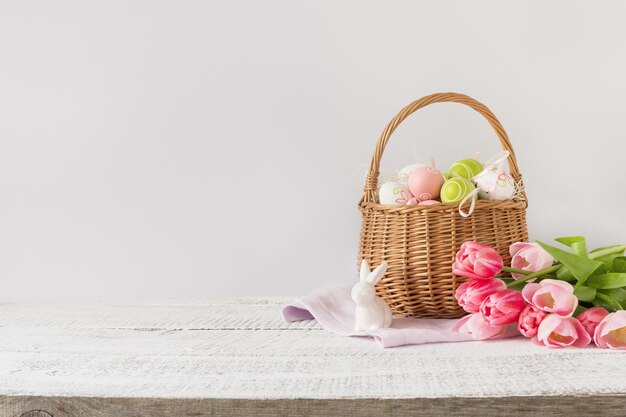 Cesto di vimini con uova di Pasqua e tulipani rosa. Fondo rosa di Pasqua della primavera con spazio per testo.