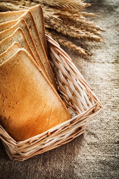 Cesto di vimini fette di pane tostato spighe di grano su tela da imballaggio