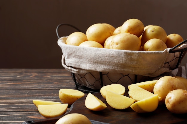 Cesto pieno di patate fresche, tavola, asciugamano e coltello su sfondo di legno, vista dall'alto