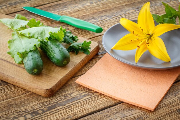 Cetrioli appena raccolti e insalata verde sul piatto del coltello del tagliere e sul fiore del giglio