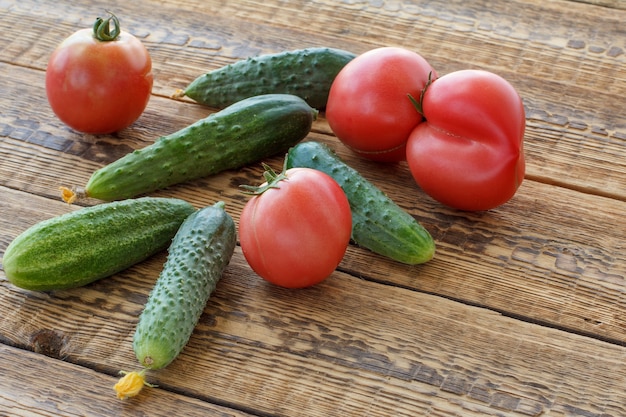 Cetrioli freschi e pomodori raccolti in giardino su vecchie tavole di legno. Verdure fresche. Vista dall'alto.