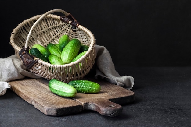 Cetrioli freschi in cesto di vimini su tavola di legno su sfondo nero.