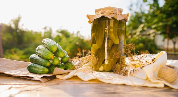 Cetrioli sottaceto salati in un barattolo su un tavolo di legno in giardino Erbe di cetrioli aneto aglio Conservazione Conservazione Spazio copia sfondo Giornata soleggiata e luminosa