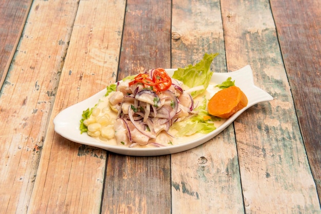 Ceviche di corvina peruviana marinata con chicchi di mais cipollotto patata dolce e lattuga in un piatto a forma di pesce