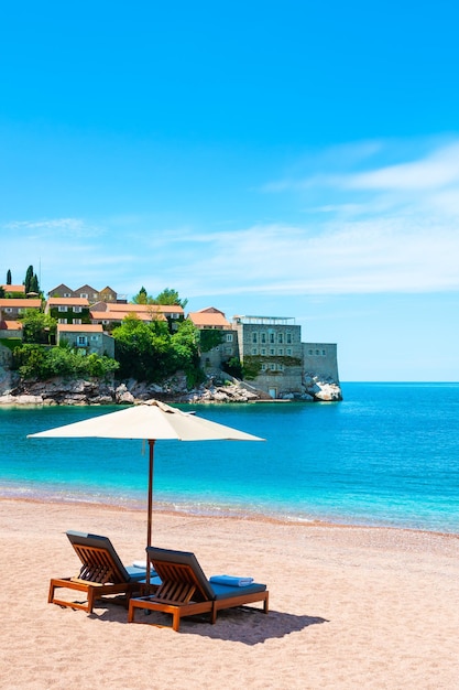 Chaise longue con ombrellone sulla spiaggia di Sveti Stefan vicino a Budva, Montenegro. Resort di lusso sul mare Adriatico.