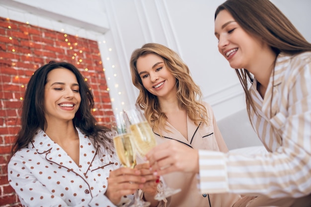 Champagne. Tre ragazze che hanno pigiama party e bevono champagne