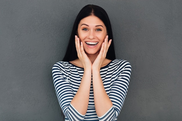 Che sorpresa! Giovane donna sorpresa che si tocca il viso e sorride stando in piedi