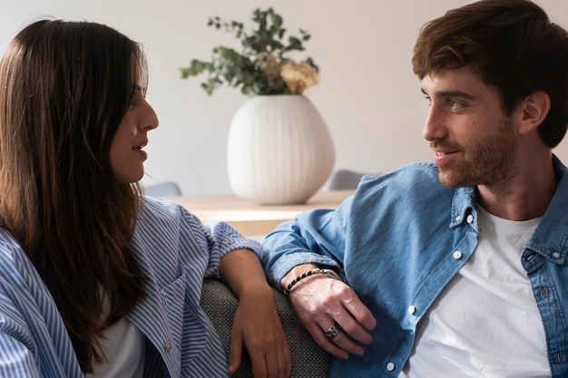 Cheerful millennial amanti interrazziali che si godono il tempo insieme a casa felice uomo arabo e donna indiana seduti sul divano nel soggiorno abbracciandosi e avendo conversazione relazione familiare d'amore