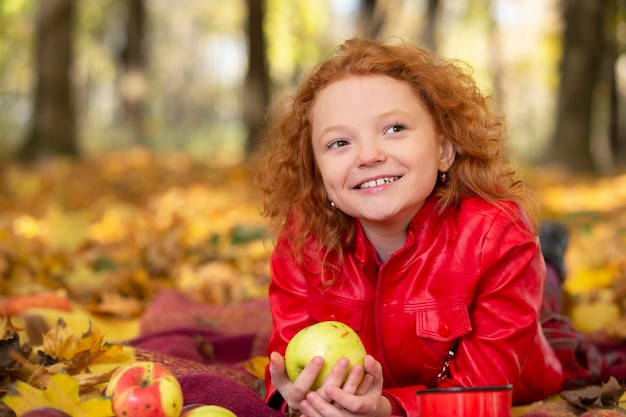 Cheerful ragazza dai capelli rossi con una mela nel parco d'autunno