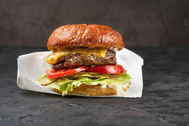 Cheeseburger con carne alla griglia, formaggio, pomodoro e patate su una superficie di pietra scura. Ideale per la pubblicità. Primo piano per il menu