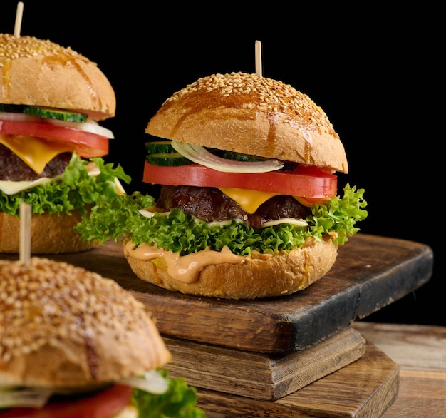 Cheeseburger con tortino di manzo alla griglia, formaggio cheddar, pomodoro e lattuga su una tavola di legno, sfondo nero