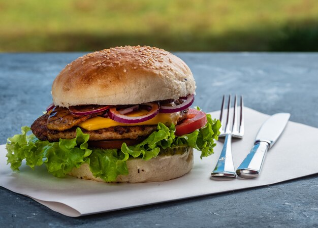 Cheeseburger saporito succoso con anelli di manzo, lattuga, sottaceti, pomodoro e cipolla su un tavolo di legno. Cibo di strada classico - hamburger alla griglia