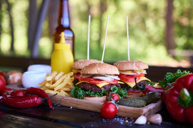 Cheeseburger serviti con patatine fritte e verdure su un tavolo di legno su un tavolo da picnic all'aperto