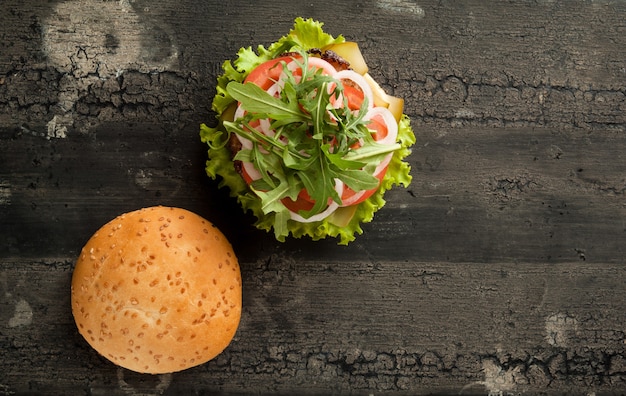 Cheeseburger su una vecchia superficie di legno di hamburger di colore scuro con carne e pomodoro su un vecchio legno