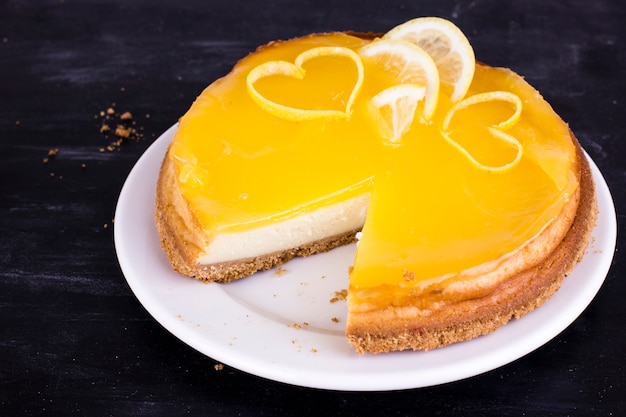 Cheesecake al limone su fondo nero decorato con la scorza di limone si chiuda