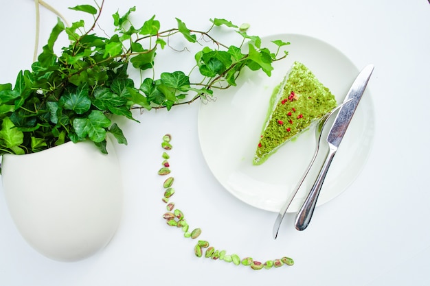 Cheesecake al pistacchio su un piatto bianco e un tavolo bianco con un vaso verde